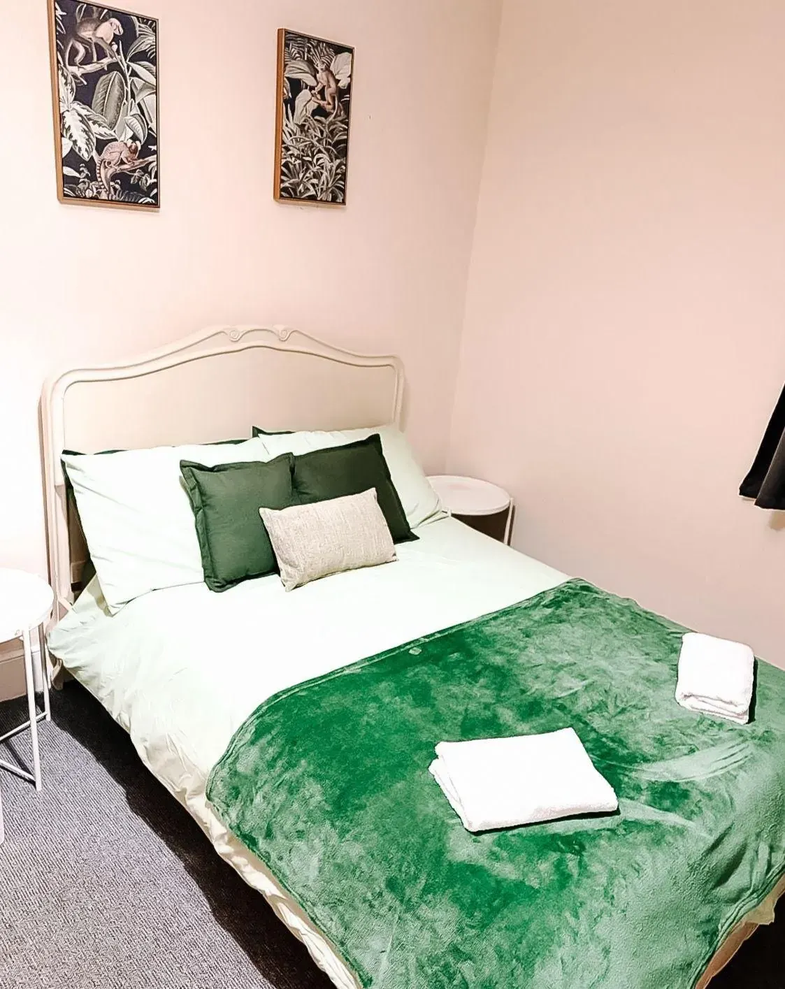 Bedroom with a green throw, white linen and framed botanical prints